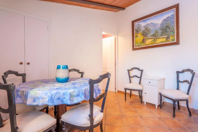 A dining area with a round table, chairs, and a framed landscape painting.