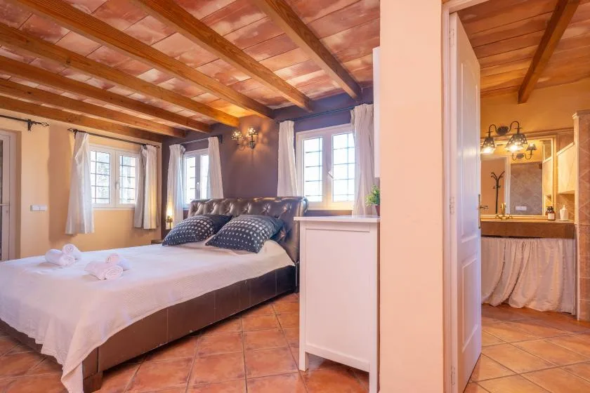 A bedroom with a large bed, exposed wooden ceiling beams, and an adjoining bathroom.