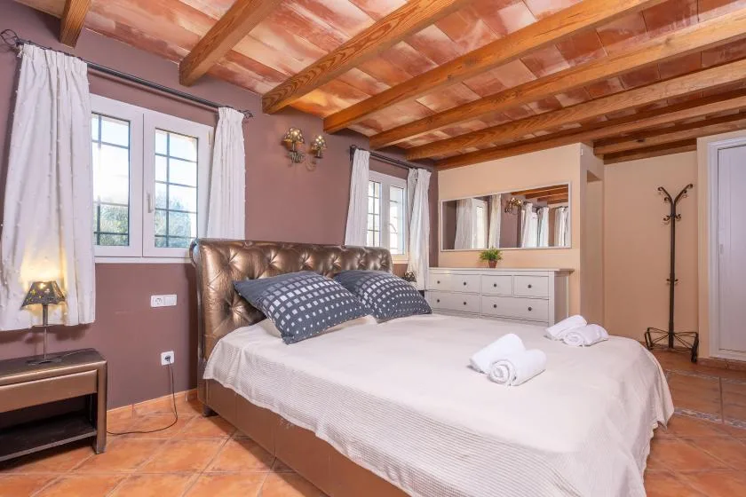 A bedroom with a large bed, white bedding, and exposed wooden ceiling beams.