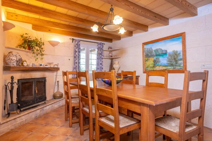 A rustic dining room with a wooden table and chairs beside a fireplace.