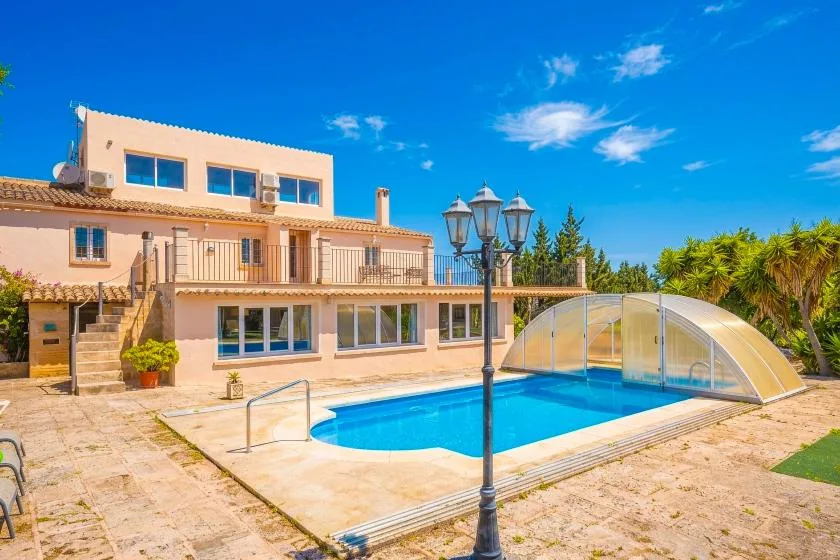A swimming pool sits beside a large villa, with a curved transparent cover.