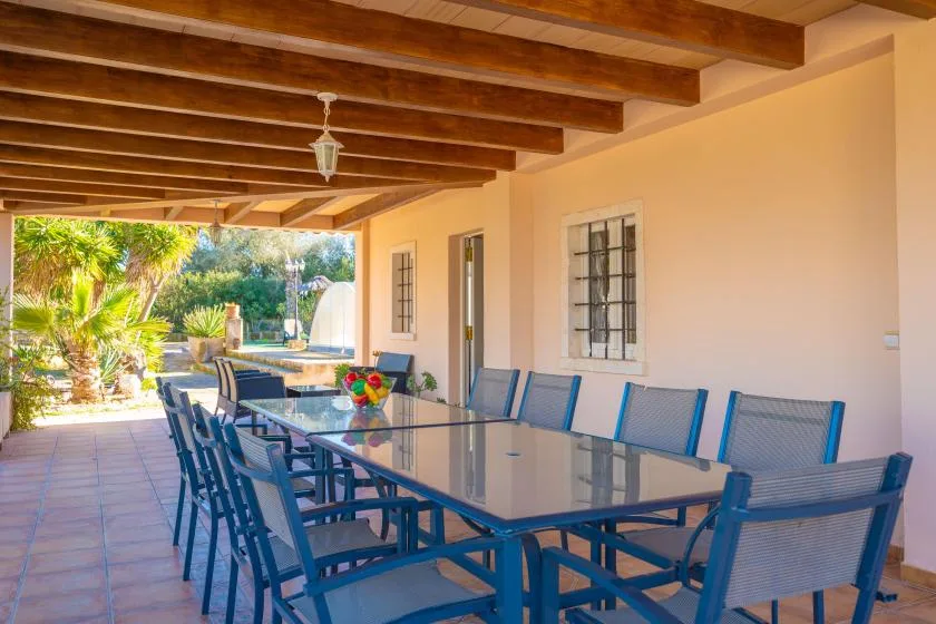 A covered outdoor dining area has a long table and blue seating.