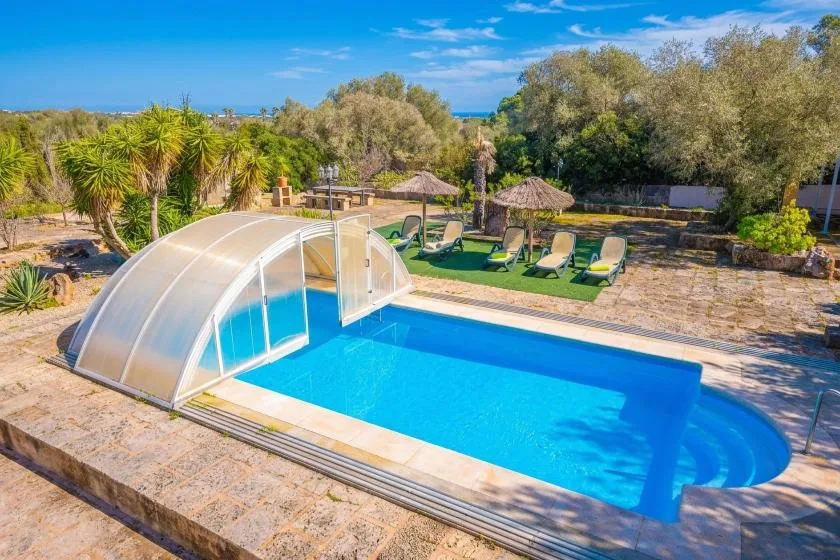 An outdoor swimming pool with a curved cover and lounge chairs nearby.