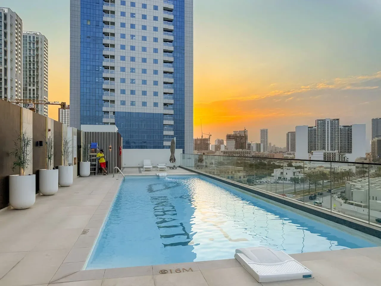 Una piscina en la azotea ofrece vistas de edificios urbanos bajo un cielo colorido al atardecer.