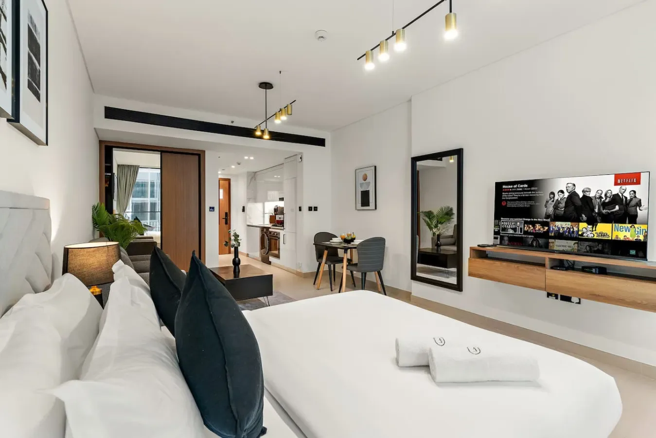 Un dormitorio moderno con una cama grande, almohadas oscuras y un televisor en la pared.