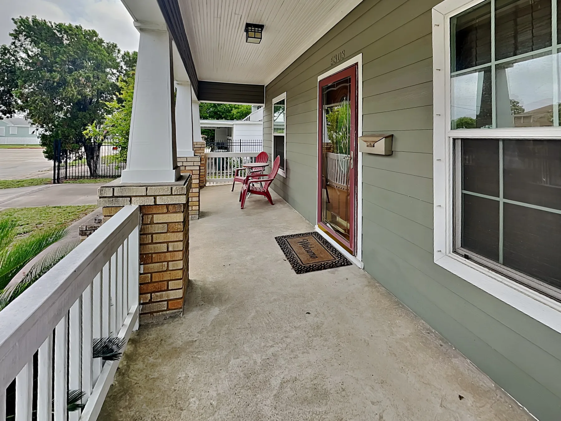 A covered porch with a red entrance door and outdoor seating.