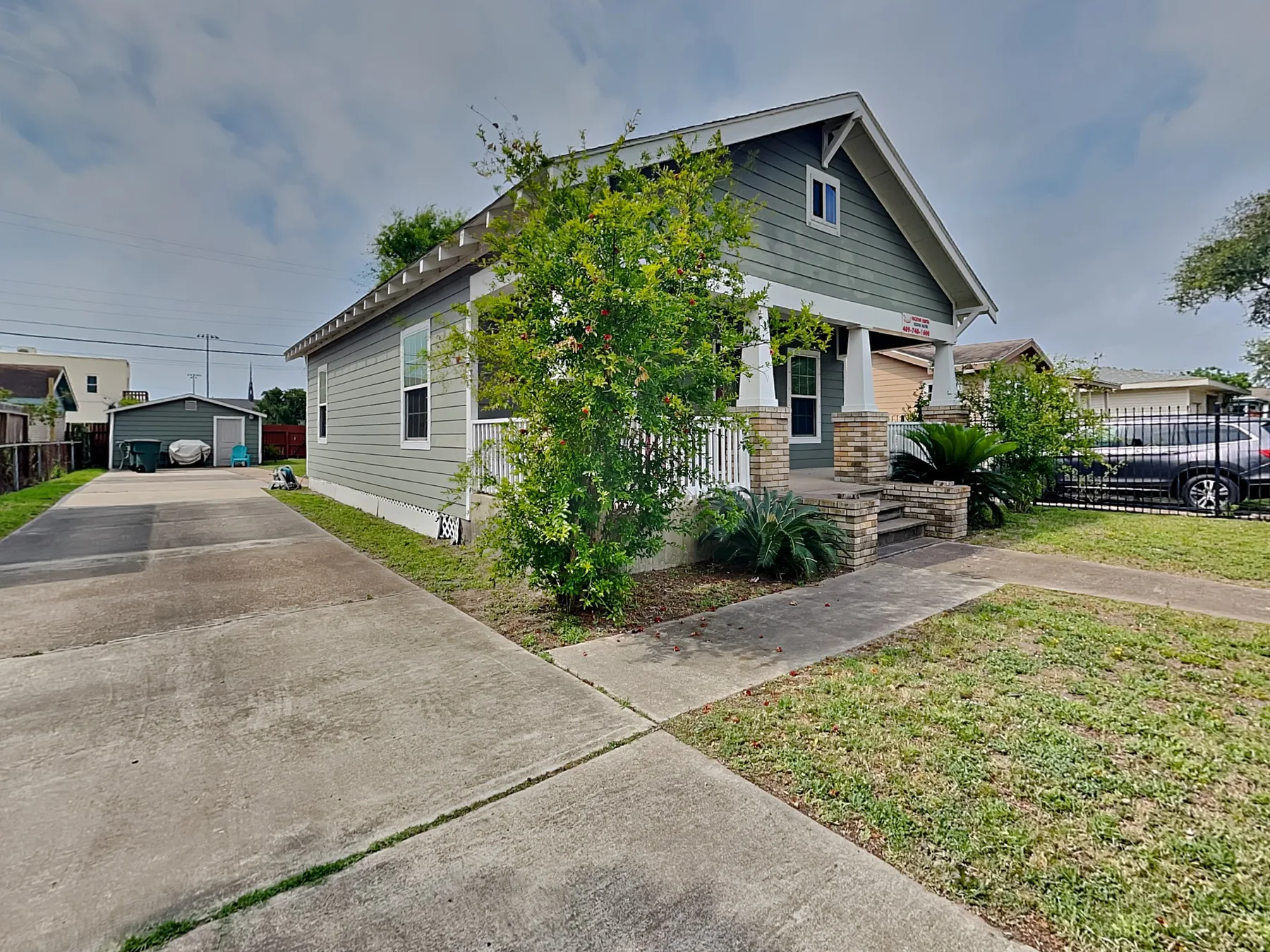 A small gray house stands beside a concrete driveway and front yard.