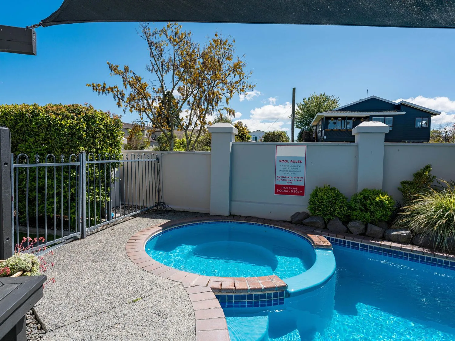 Una zona de piscina al aire libre con una pequeña piscina de hidromasaje redonda junto a una piscina más grande rodeada de una superficie de hormigón y una valla metálica en Sun and Swim - Lake Taupo Holiday Home, en Taupo Central.