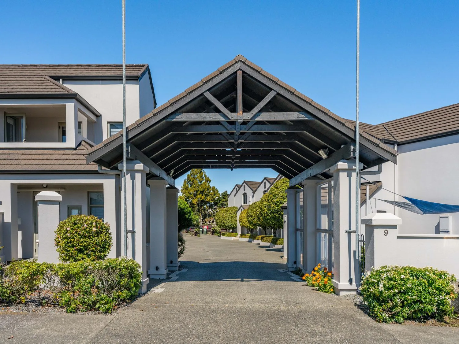 A covered entrance frames a paved driveway between buildings and landscaped shrubs.