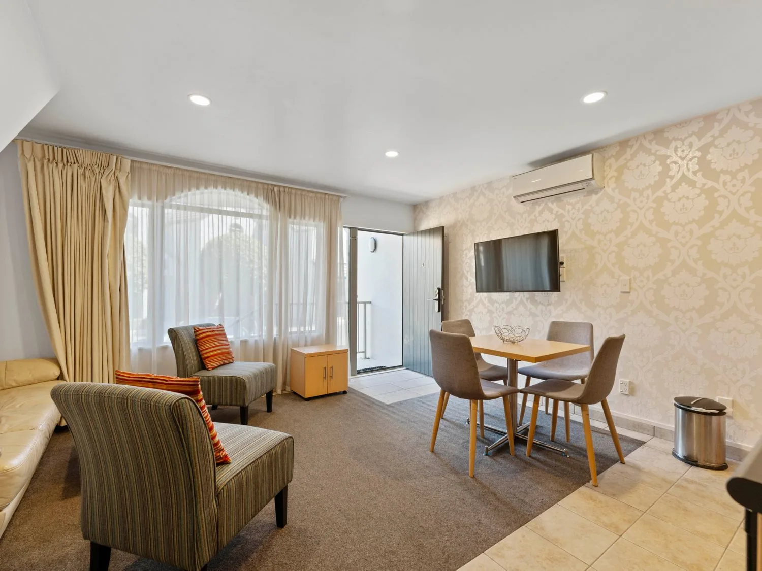 Una sala de estar con sillas, una mesa y un televisor montado en la pared en Sun and Swim - Lake Taupo Holiday Home, en Taupo Central.