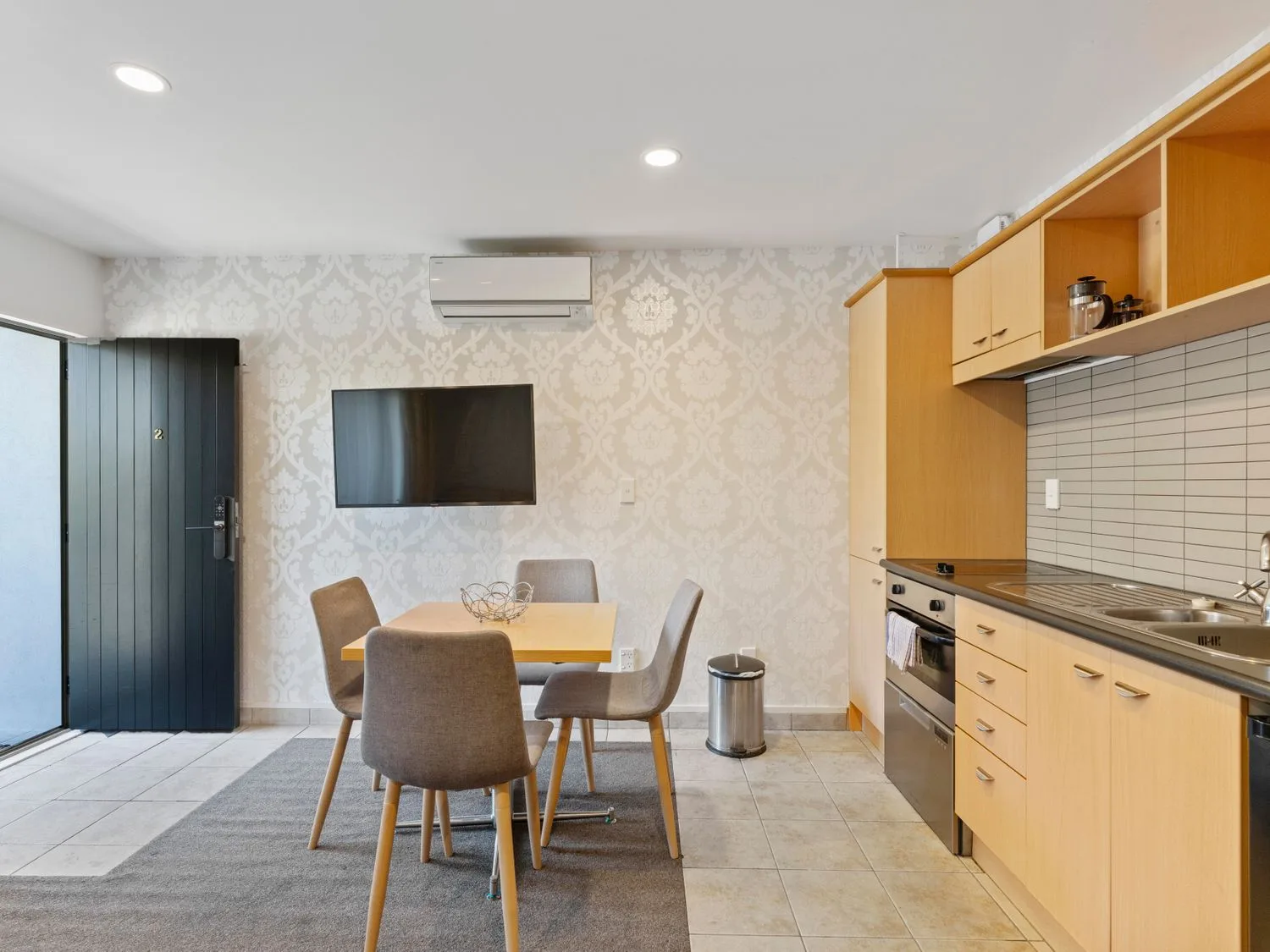 A dining area with a wooden table and four chairs next to a kitchen with wooden cabinets and appliances at Sun and Swim - Lake Taupo Holiday Home in Taupo Central
