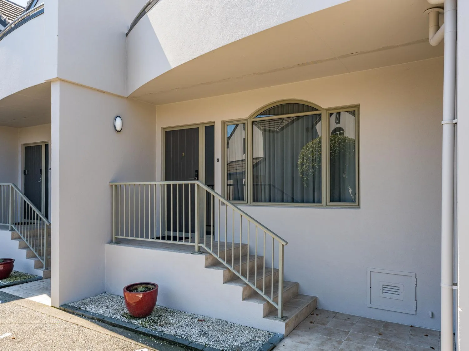 A building entrance with steps, a railing, a door, and a curtained window.