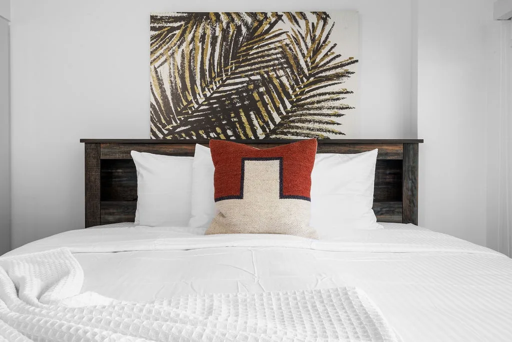 Settle into your peaceful retreat with a plush bed and rustic wood headboard, where crisp linens and tasteful artwork create the perfect haven for rest.