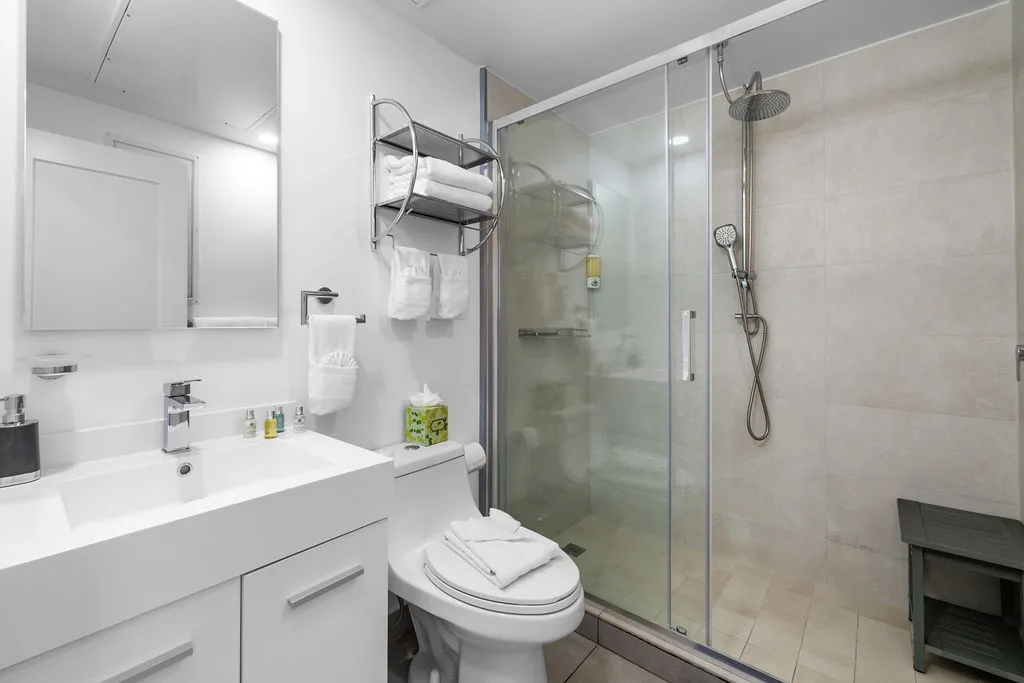 Your modern bathroom features a spacious walk-in shower with rainfall showerhead, crisp white vanity, and fluffy towels waiting for you after a refreshing rinse.