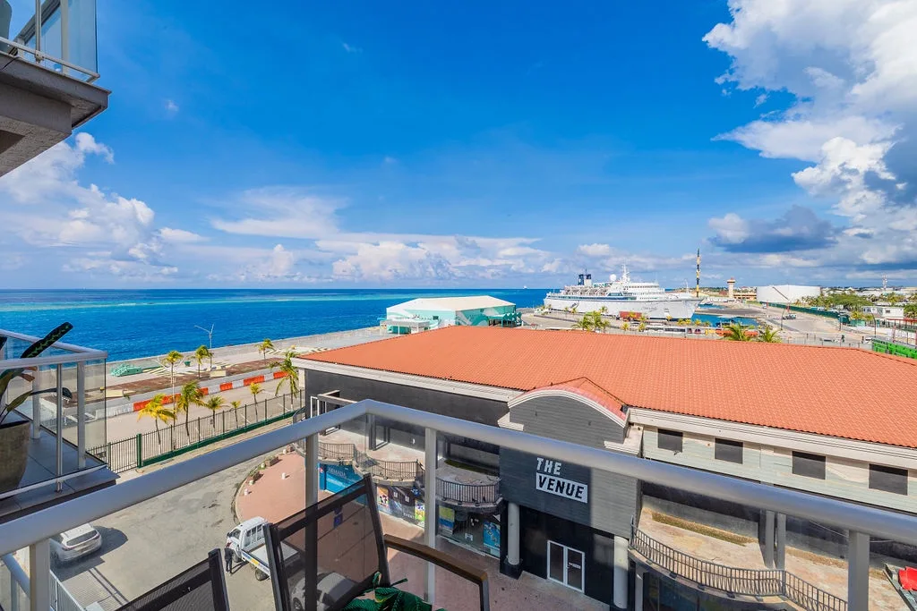 Sweeping coastal views stretch from the balcony, showcasing vibrant blue waters, nearby port activity, and the surrounding island neighborhood under open skies.