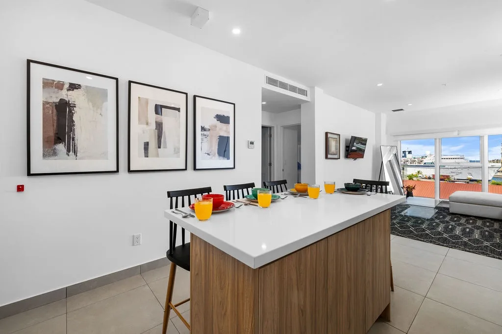 Gather around your bright, modern kitchen island for breakfast with colorful place settings, enjoying natural light and city views through large windows that frame your stay.