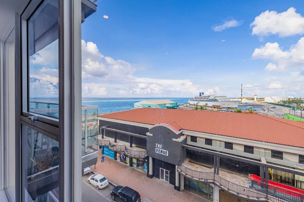 Coastal property overlooking a marina with cruise ship access and local shopping venues. Balcony view captures the harbor area and surrounding waterfront district.