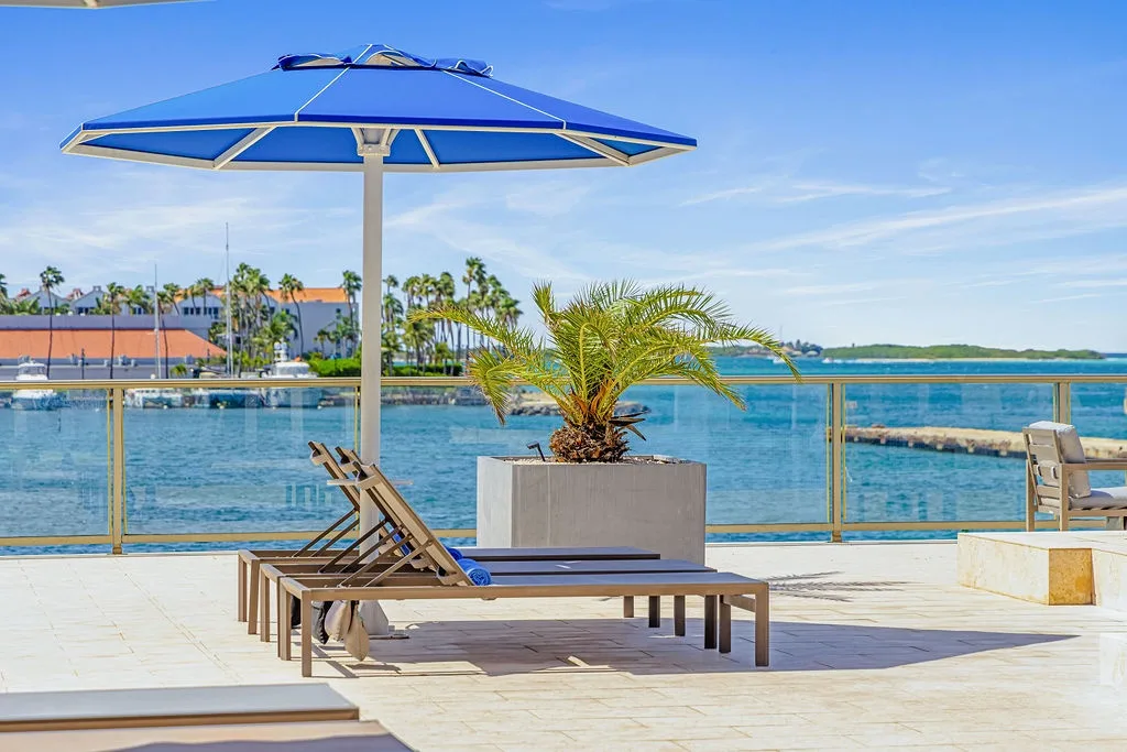 Waterfront deck with loungers offering stunning views of sparkling turquoise waters, swaying palms, and distant shores under a brilliant blue sky.