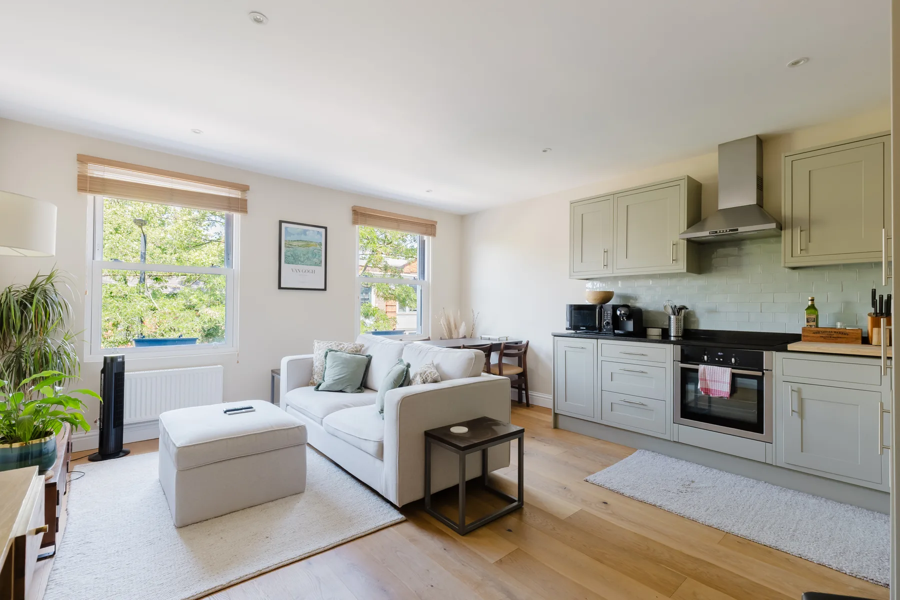 A bright living area opens into a kitchen, with a sofa beside the windows.