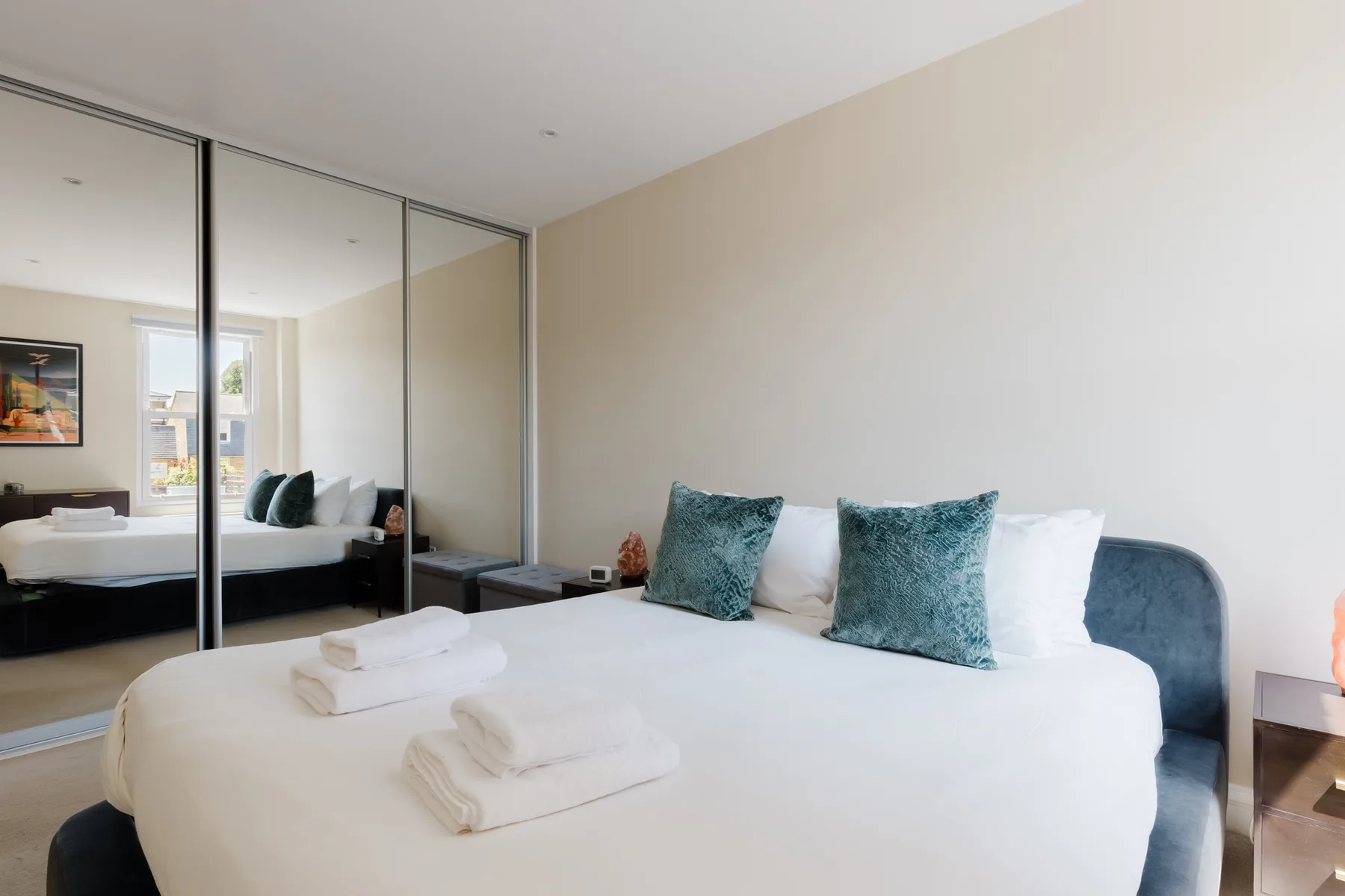 A bedroom with a bed, teal pillows, and mirrored closet doors.