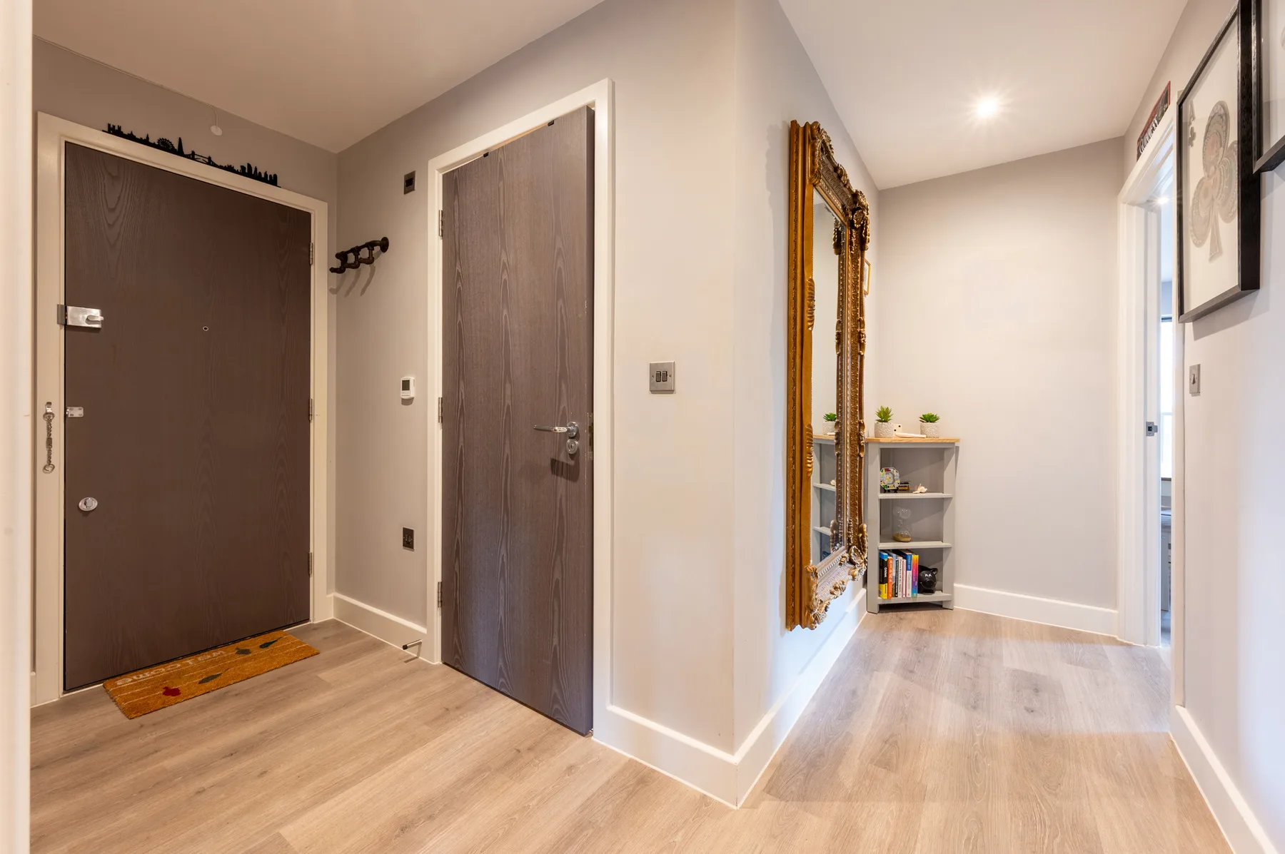 Un pasillo interior con dos puertas, un espejo y una pequeña estantería.