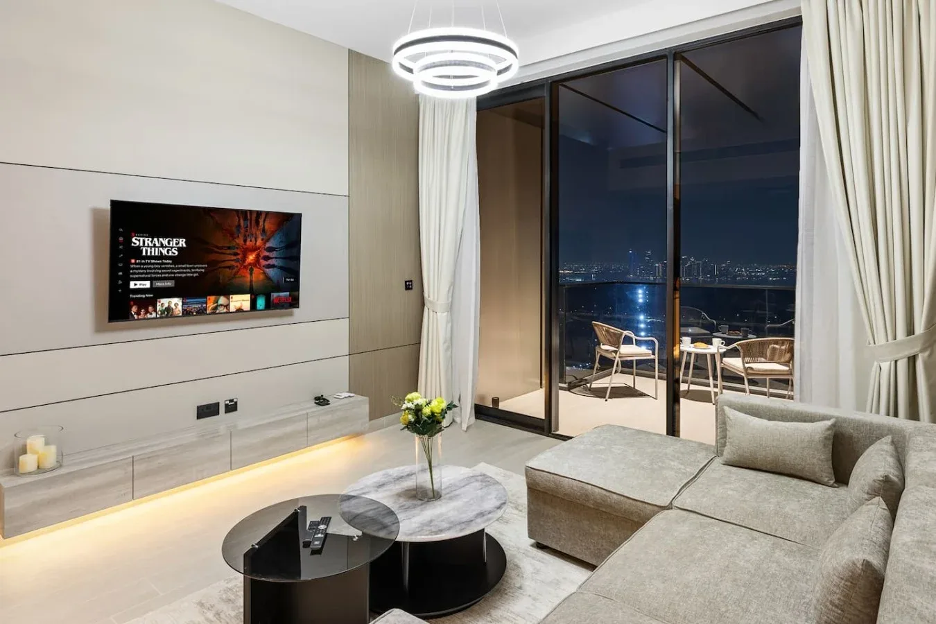 Una sala de estar moderna con zona de descanso, televisor en la pared y grandes puertas de vidrio.
