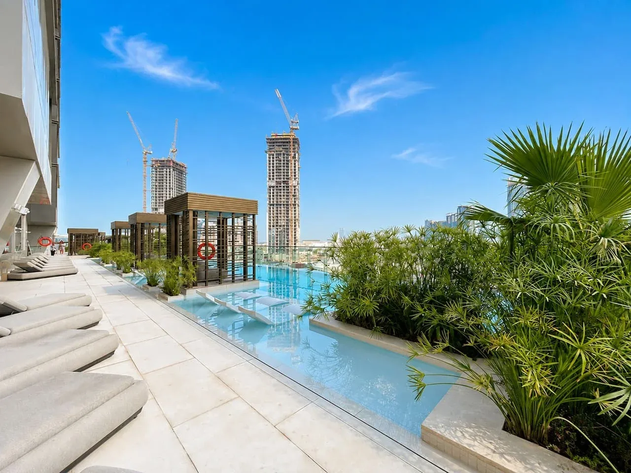 Una piscina al aire libre junto a tumbonas acolchadas y vegetación.