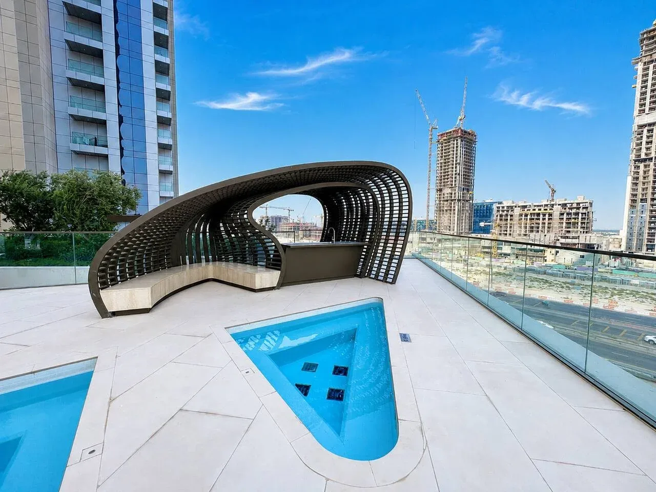Una piscina en la azotea y una zona curva de asientos con sombra miran hacia edificios cercanos en construcción.
