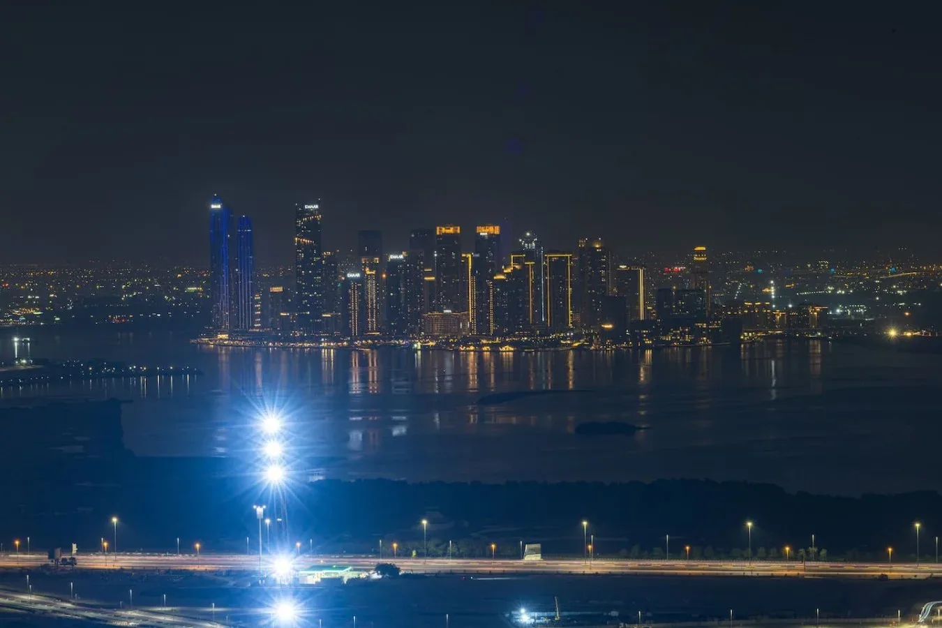 Un horizonte urbano nocturno brilla al otro lado del agua, con luces reflejadas en la superficie.