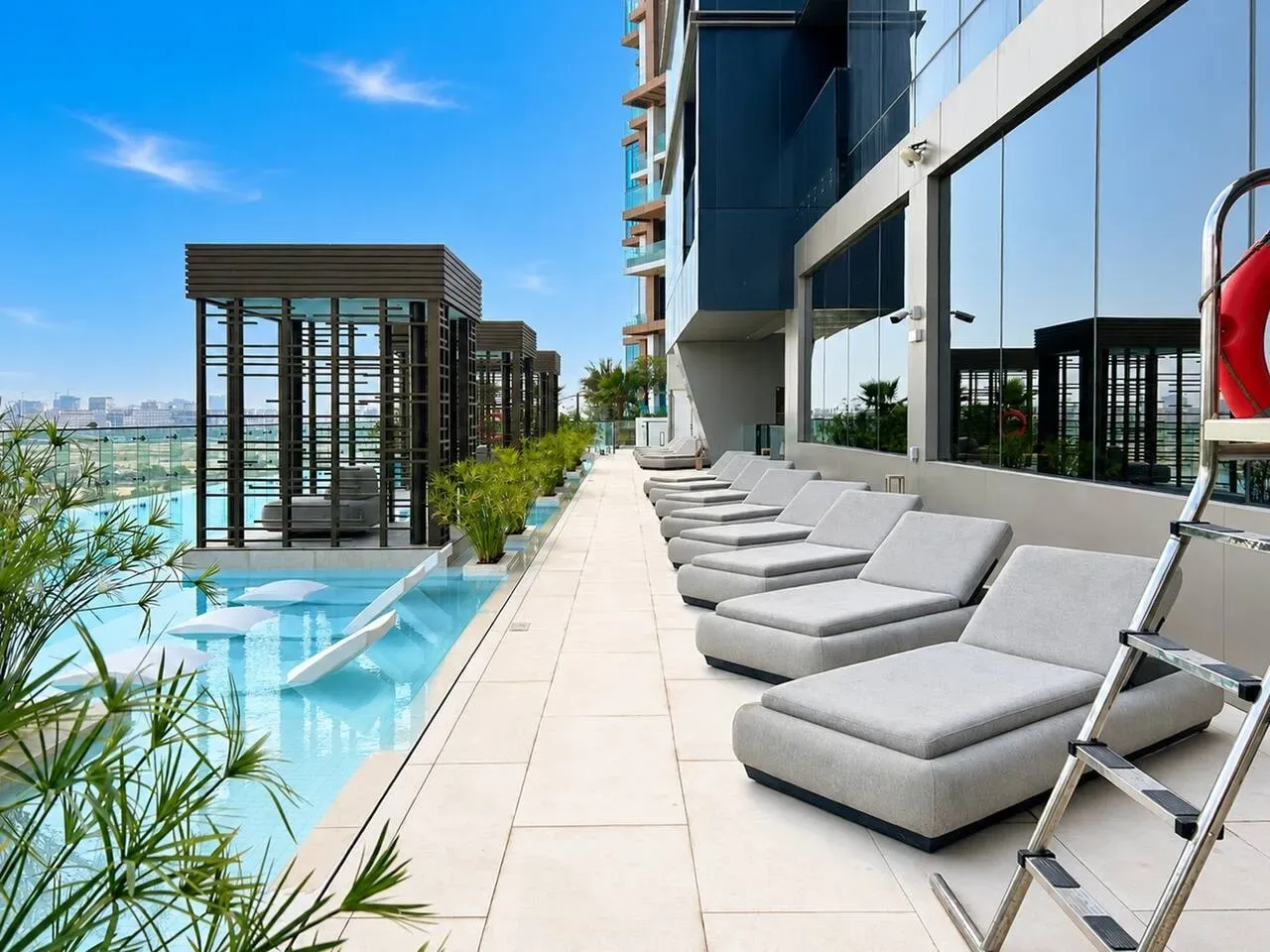 Una terraza soleada junto a la piscina, con tumbonas al lado de un edificio moderno.