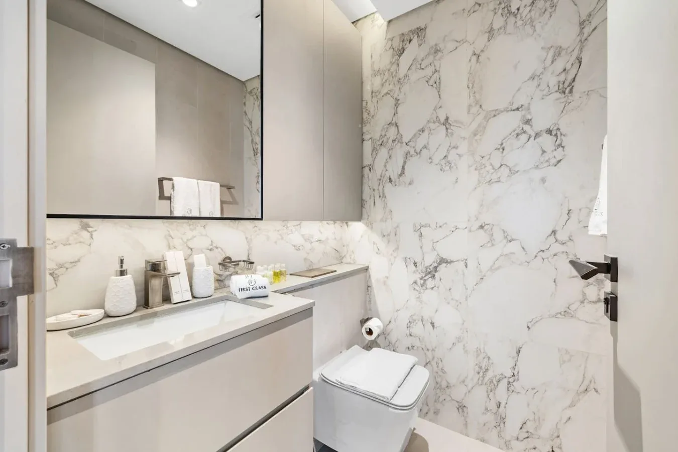 Un baño moderno con lavabo, espejo grande y paredes con vetas de mármol.