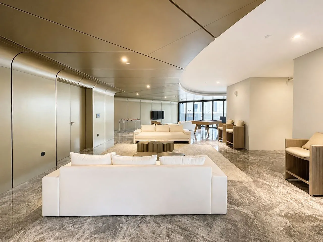 Un salón moderno con asientos claros, una mesa baja y grandes ventanas.