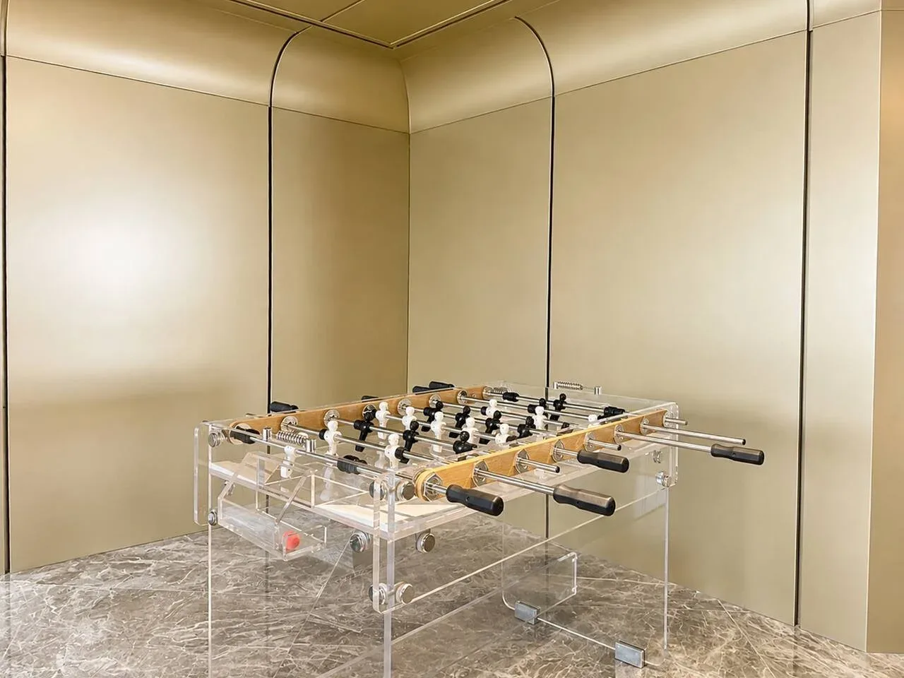 Una mesa de futbolín está en una habitación con paredes color crema y suelo con diseño de mármol.
