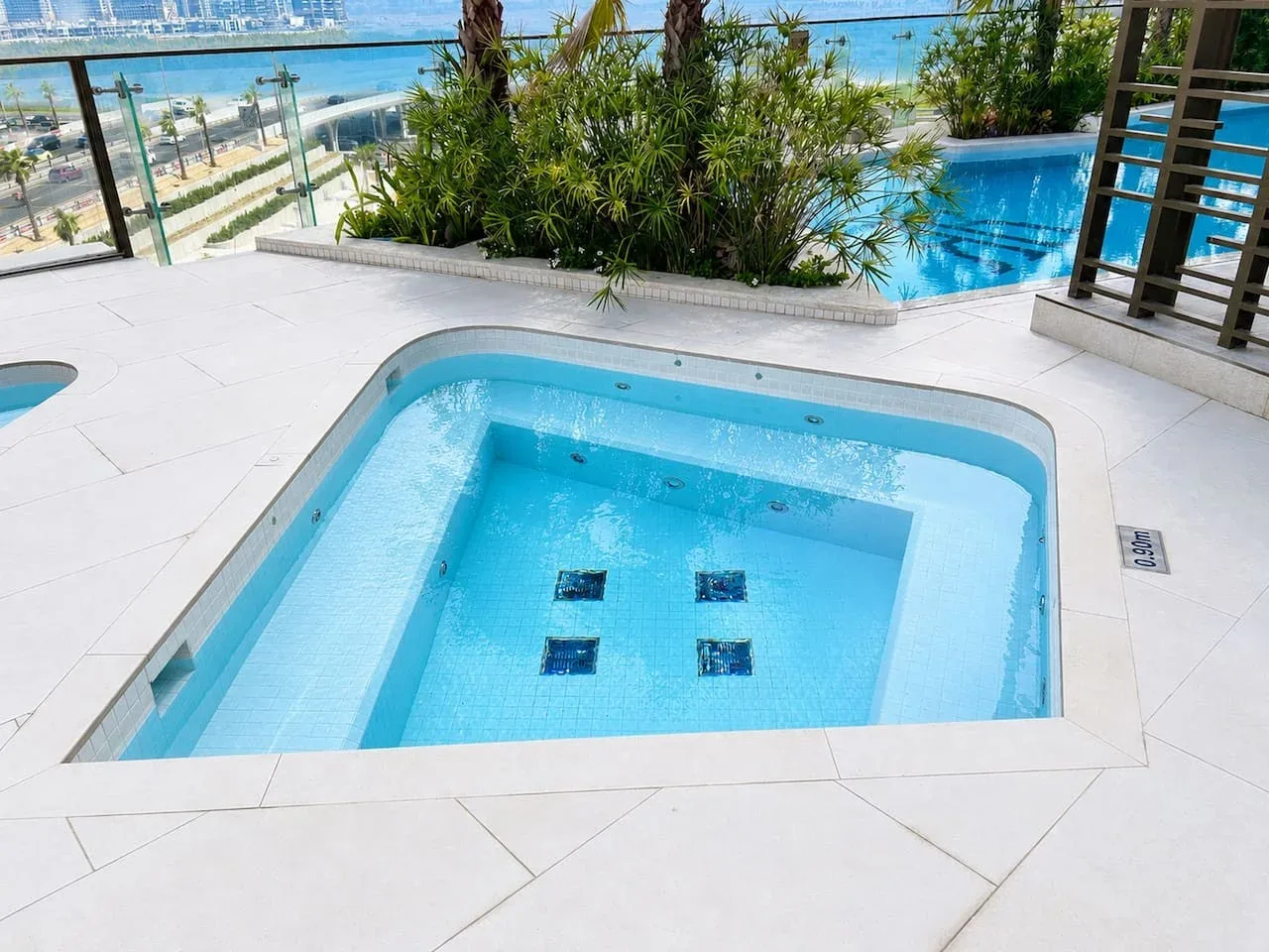 Una pequeña piscina está en una terraza luminosa, con otra piscina detrás de las plantas.
