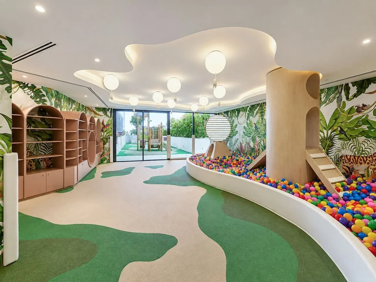 Una colorida zona de juegos interior tiene una piscina de bolas, una estructura para trepar y murales de hojas.