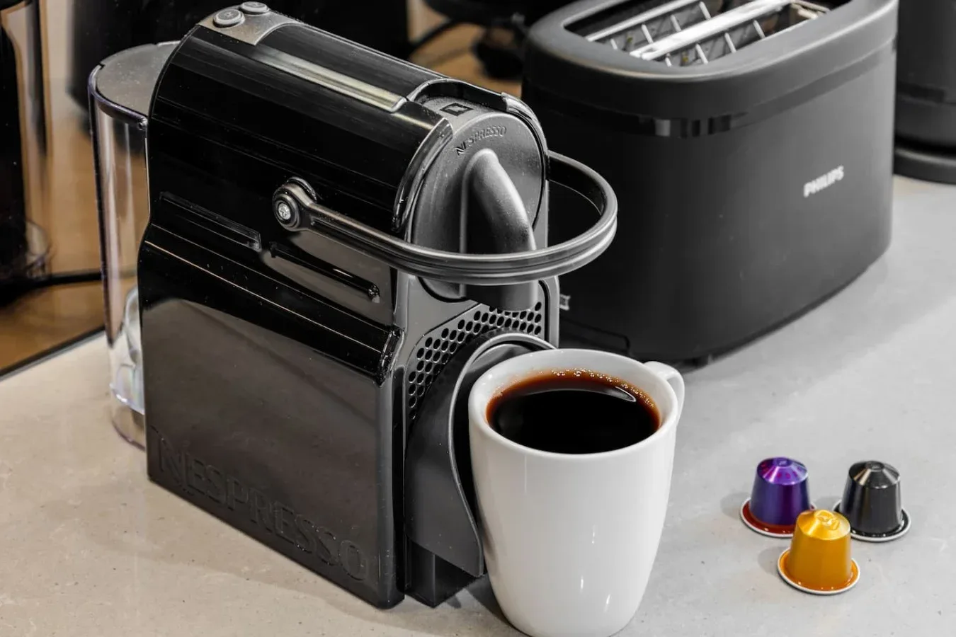 Una encimera de cocina con una cafetera, una taza de café y cápsulas.