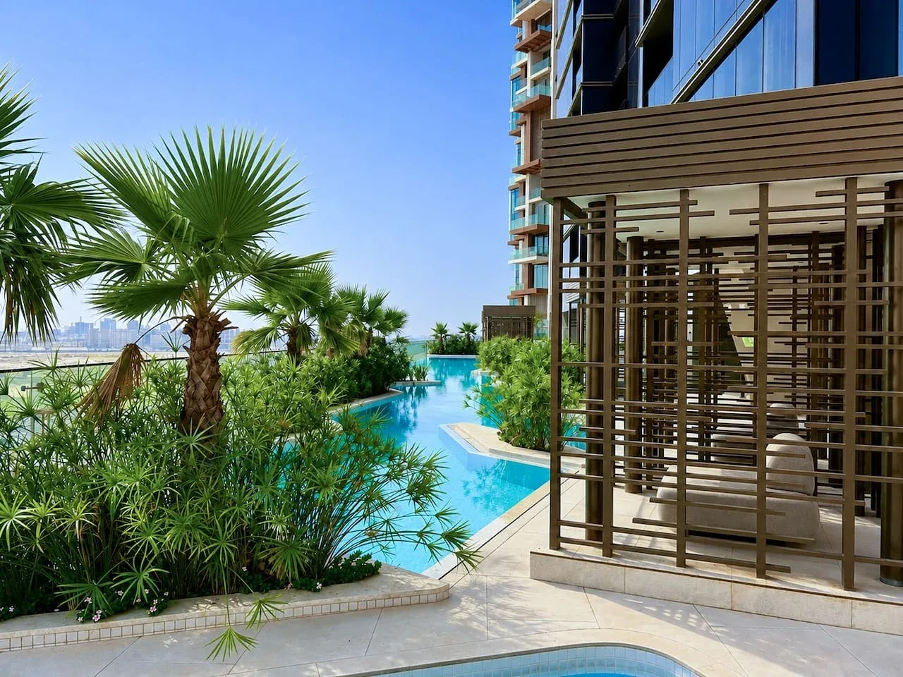 Una piscina exterior se curva entre jardines junto a un edificio moderno.