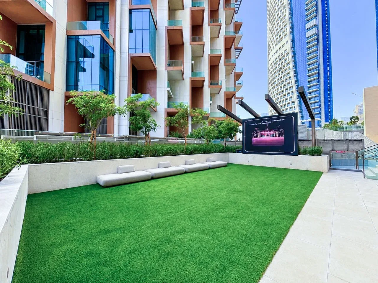 Un patio exterior con césped verde, asientos y edificios de apartamentos alrededor.