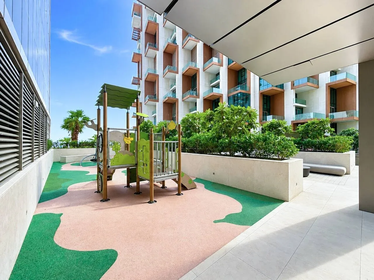 Una zona de juegos al aire libre con estructuras para trepar y jardineras junto a un edificio moderno.