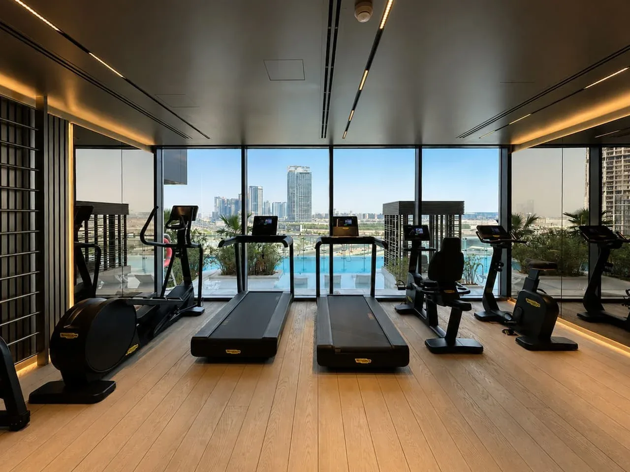 Un gimnasio con equipos de ejercicio y ventanales que dan a la ciudad.