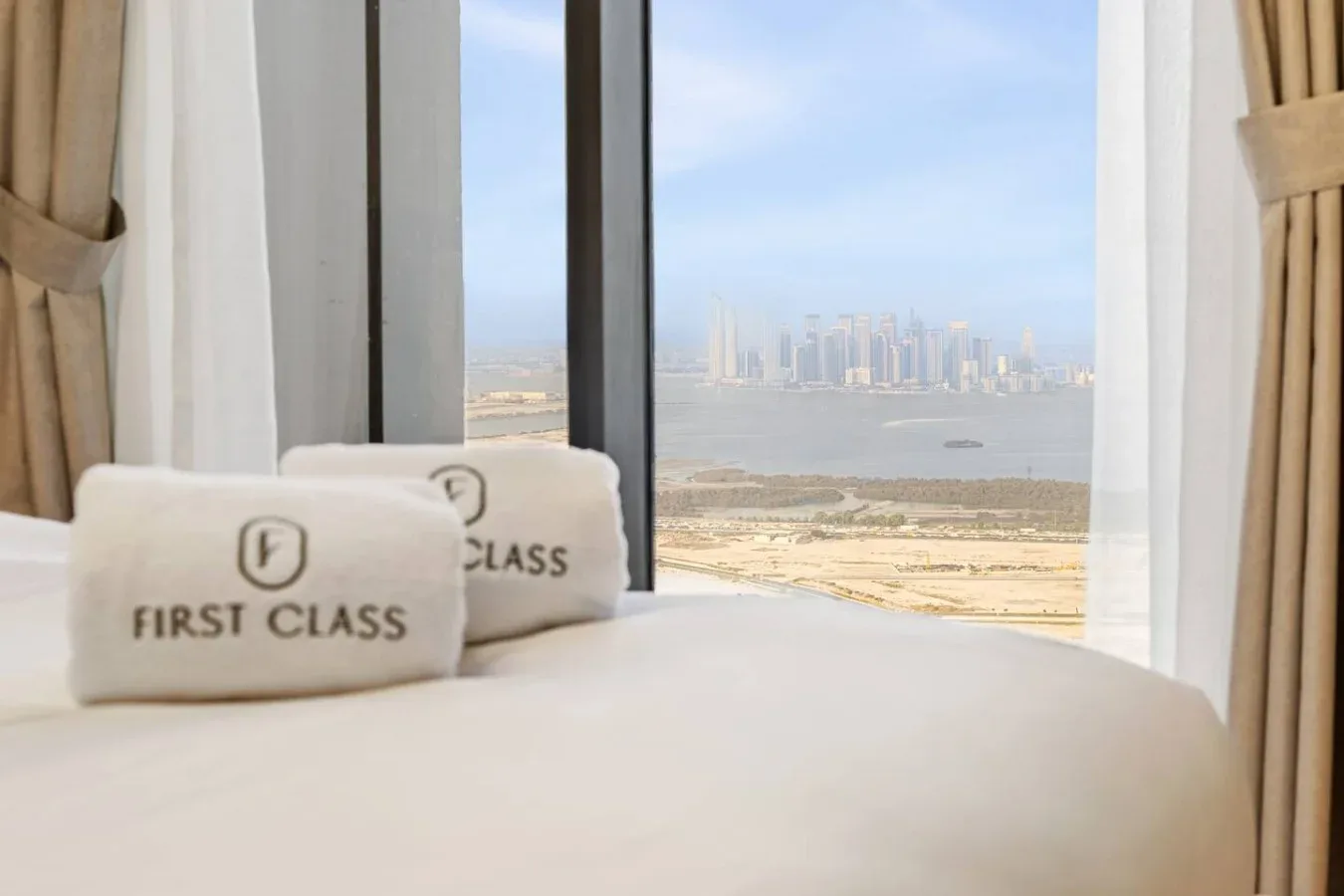 Un dormitorio con una cama junto a una ventana grande con vistas al agua y edificios lejanos.