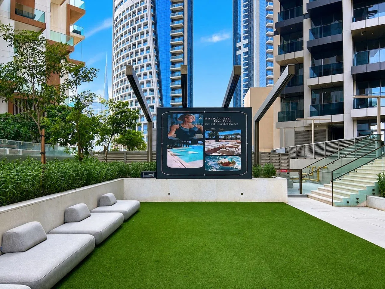 Un patio ajardinado con asientos, césped verde y edificios altos alrededor.