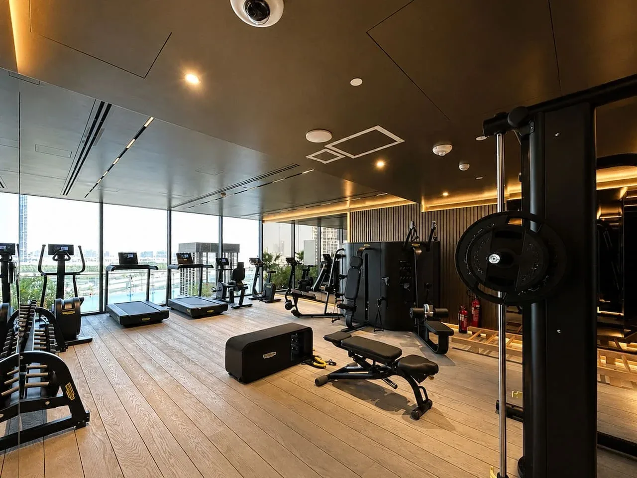 Una sala de ejercicios con máquinas y equipo de fuerza junto a grandes ventanales.