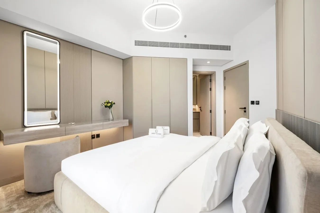 Un dormitorio luminoso con una cama bien tendida y un pequeño jarrón con flores.