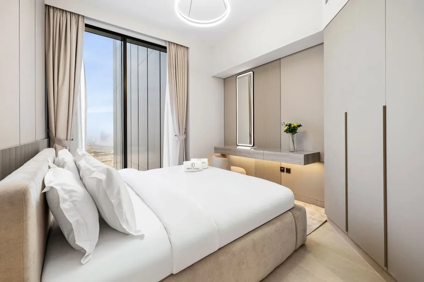Un dormitorio luminoso con una cama tendida y ventanas altas enmarcadas por cortinas.