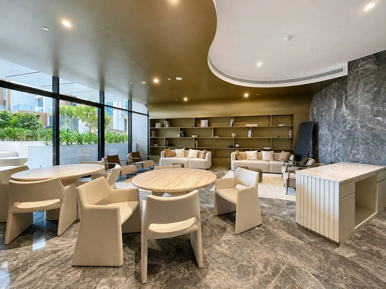 Un salón luminoso con asientos alrededor de mesas y grandes ventanales.