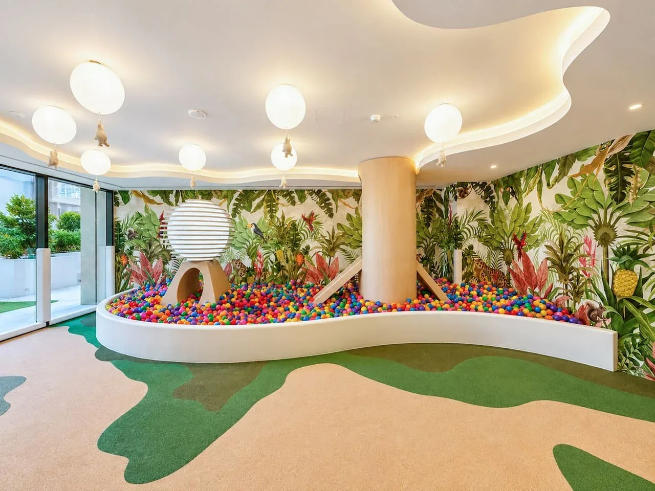 Una colorida zona de juegos interior tiene una piscina de bolas, un tobogán y un mural de hojas.