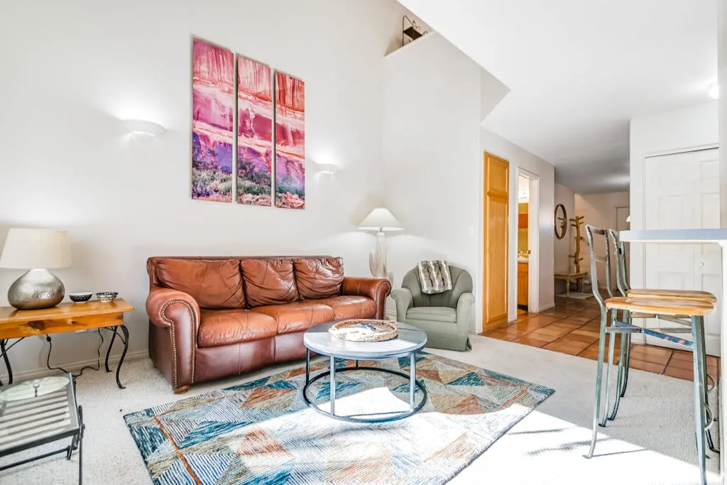 Una sala luminosa con asientos de cuero, una mesa de centro de vidrio y arte colorido en la pared.
