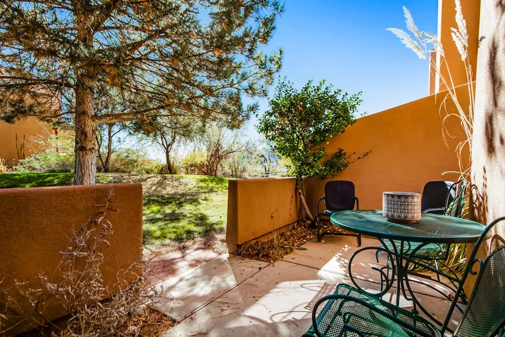 Un patio exterior con asientos y una mesa junto a paredes anaranjadas y árboles.