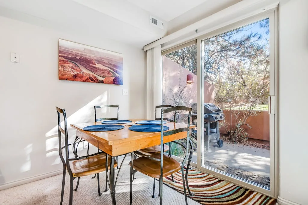 Un comedor luminoso con una mesa de madera junto a puertas corredizas de vidrio que dan a un patio.